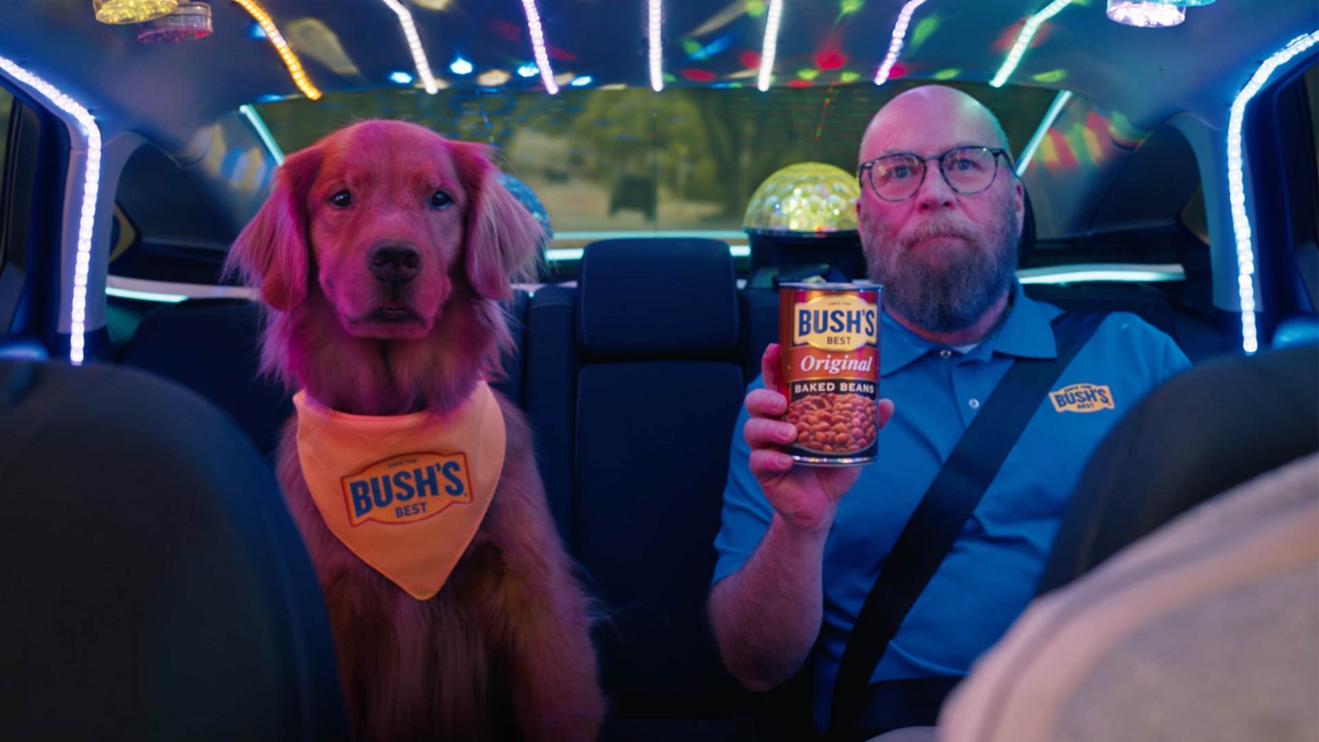 Jay Bush sits beside Duke the dog while holding a can of Bush’s Baked Beans in the back of an SUV.