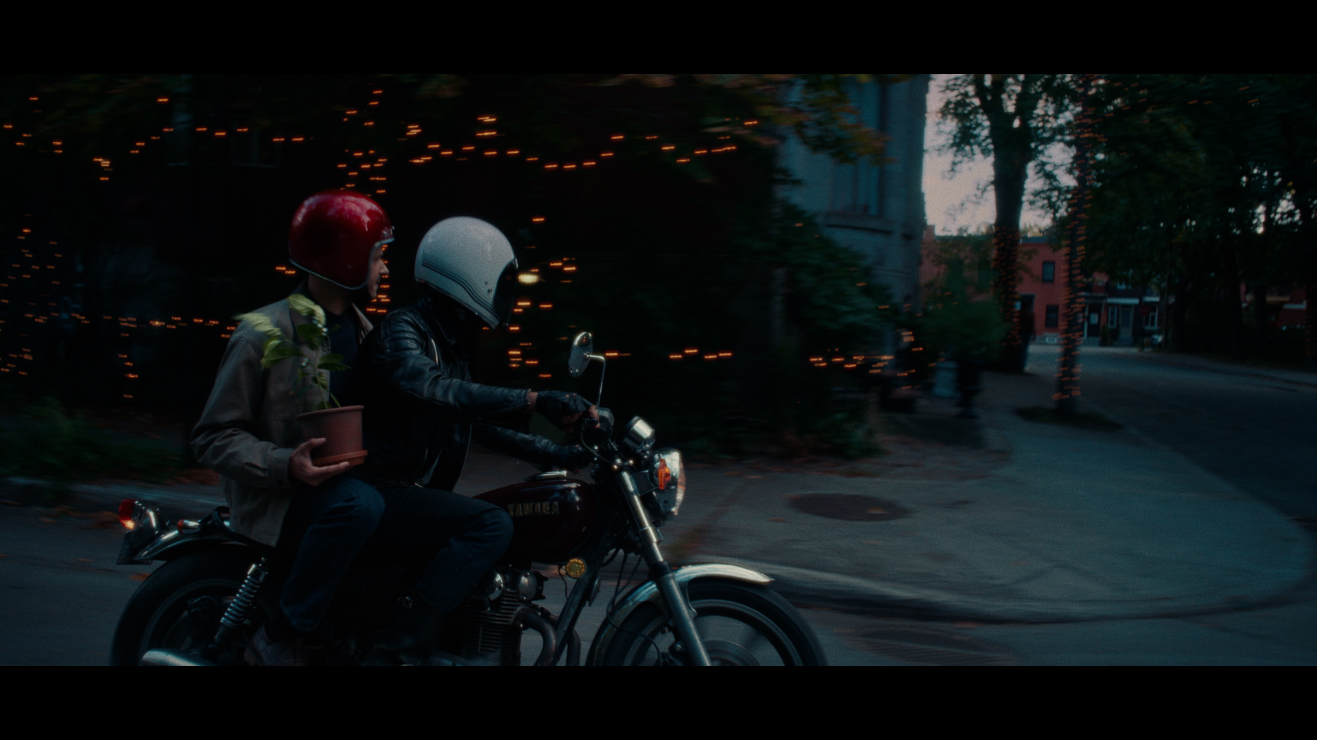 Two people on a motorcycle driving through a town.
