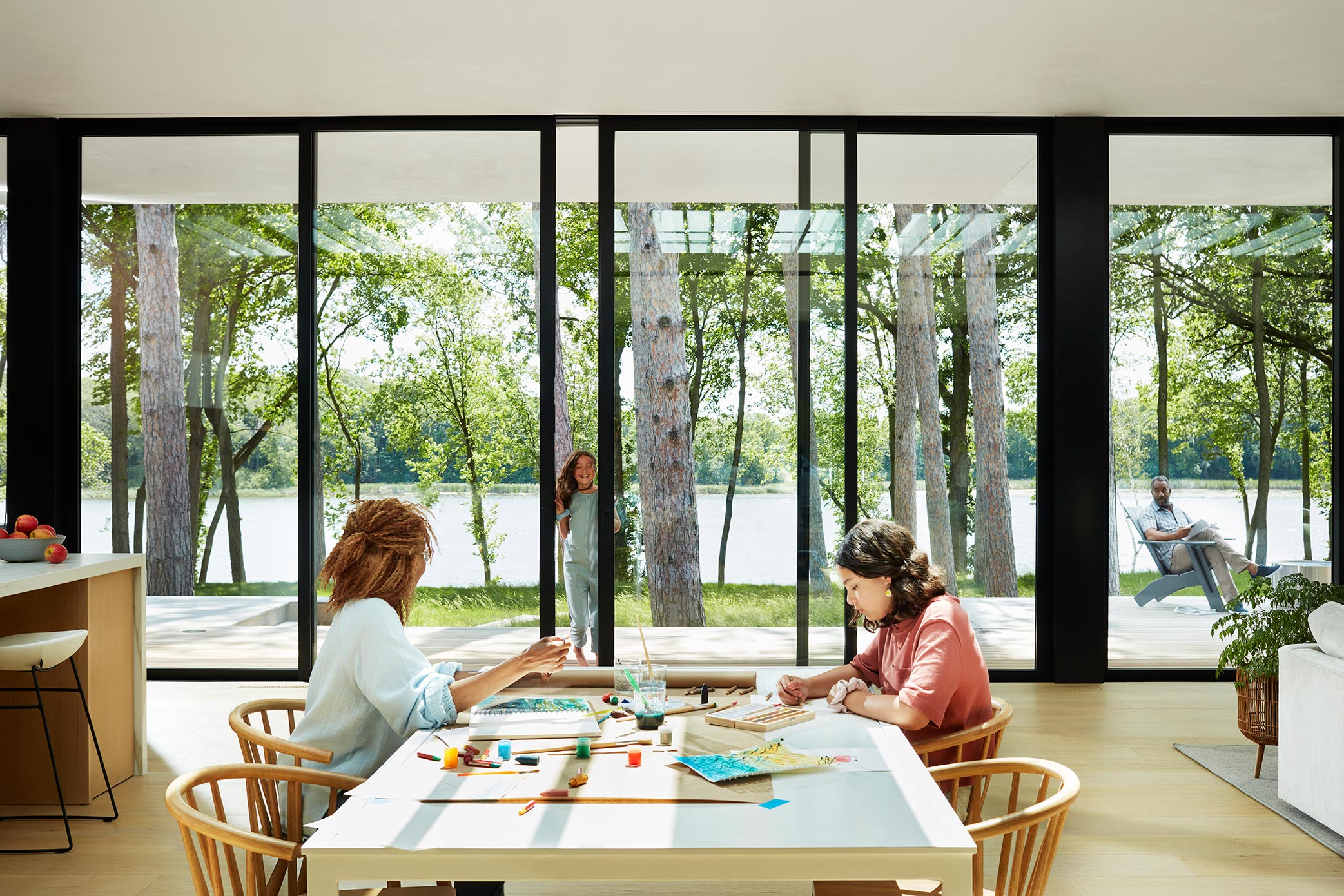 Two people sitting at the dining table with big windows and the backyard in the background.