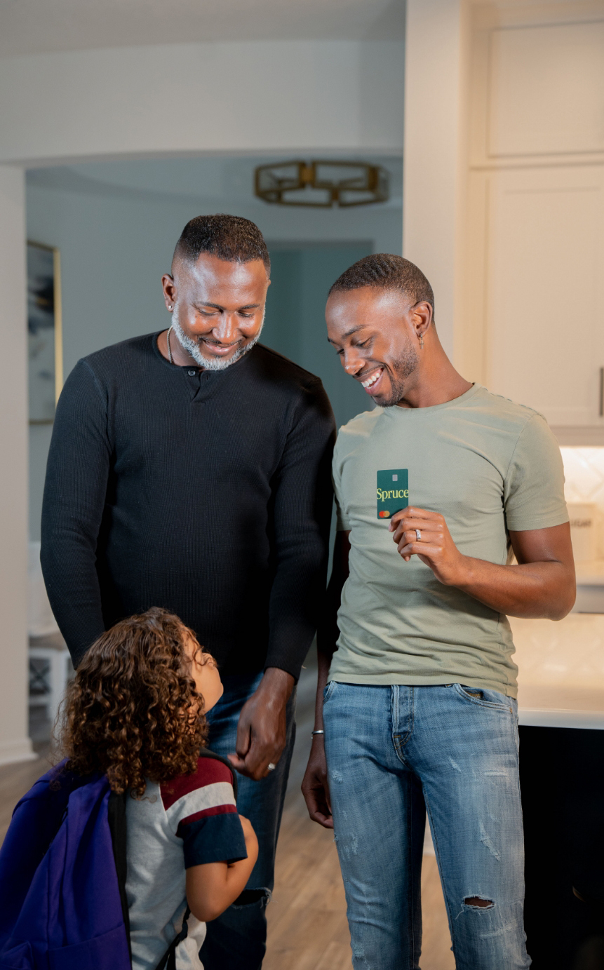 A customer holding a Spruce bank card while standing next to a man and smiling at a child.